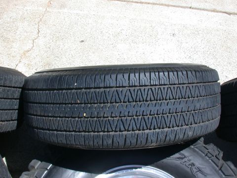1996 Ford Bronco - A spare tire is shown resting on the ground next to other tires.
