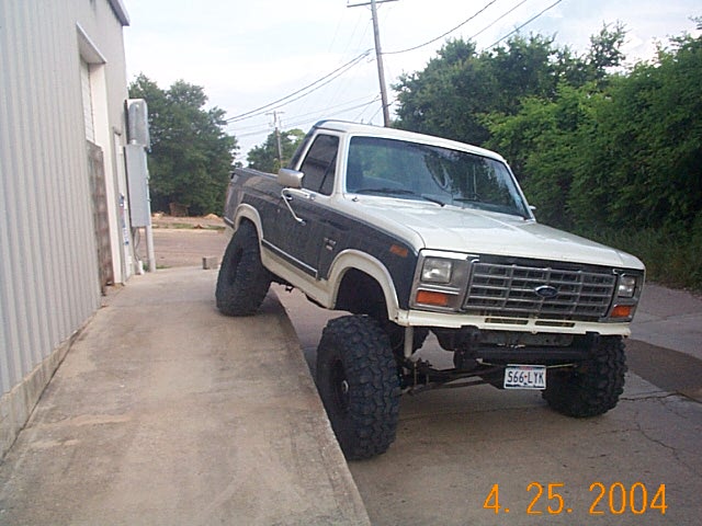Lifted white and dark two-tone Ford Bronco flexing front suspension on a curb