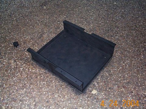 1986 Ford Bronco - A black metal tray sits on a gravelly surface, with a small black cap to its left.