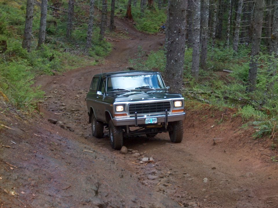 FORD full-size SUV on a muddy forest trail with a dirt bike in the background