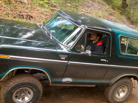 1978 Ford Bronco - A 1978 Ford Bronco navigates a dirt path, its dark green paint contrasting with the surrounding foliage.