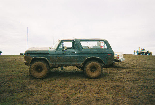 Muddy dark green Ford Bronco with white roof parked side-on in a dirt field