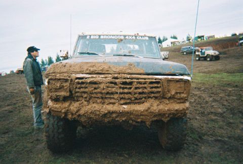 1978 Ford Bronco - Mud-covered 1978 Ford Bronco at an off-road event, with other vehicles visible in the background.