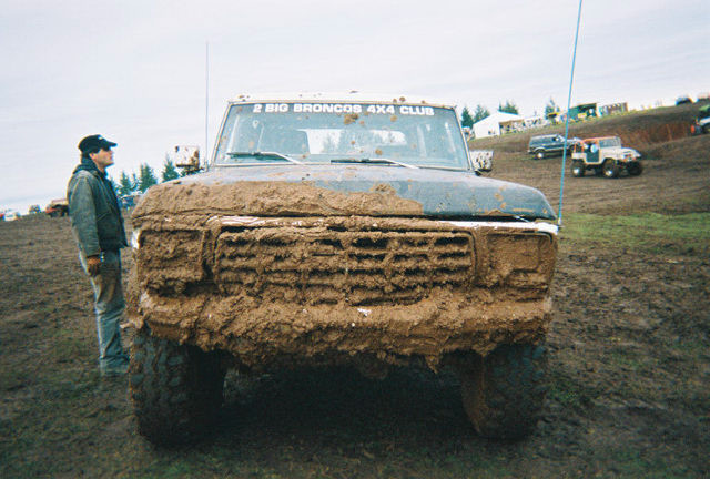 Mud-caked front end of dark Ford 4x4 with 2 Big Broncos 4x4 Club windshield banner