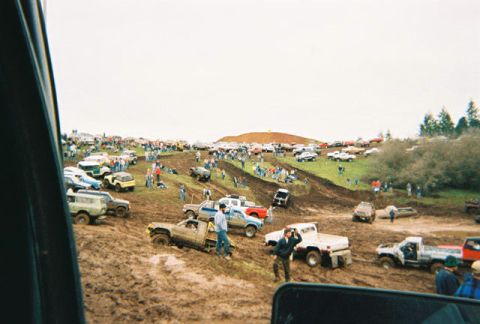 1978 Ford Bronco - Off-road vehicles navigate a muddy track during an event, with spectators watching from the sidelines.