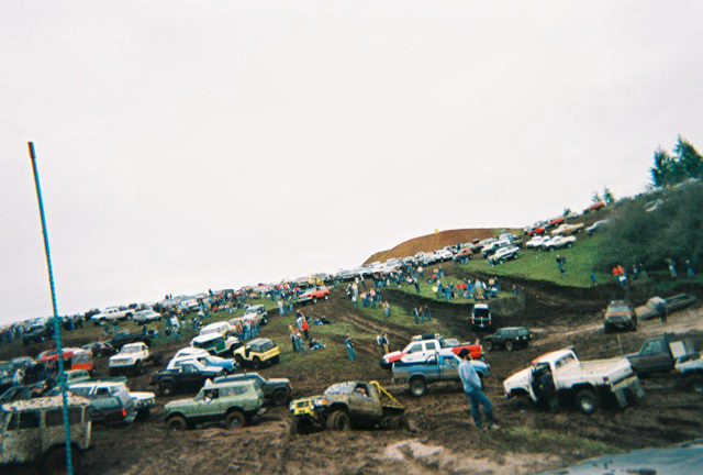 Crowd of mud-covered 4x4 trucks and SUVs staged on a grassy hillside at an off-road event
