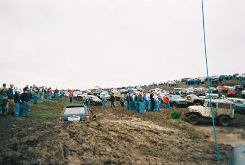 1978 Ford Bronco - A muddy scene with multiple off-road vehicles bogged down and spectators gathered around.