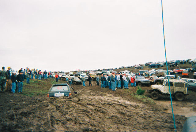 Crowd and rows of 4x4s along a muddy hillside at an off-road event