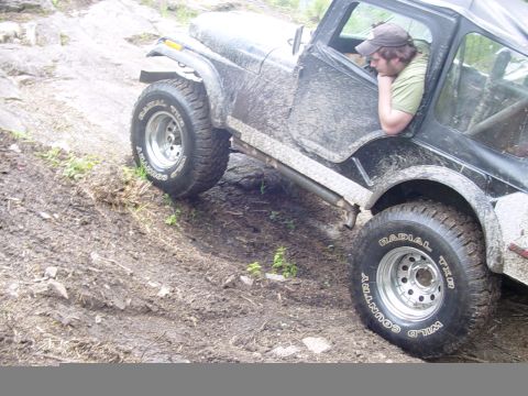 1987 Ford Bronco - A Jeep Wrangler navigates a muddy off-road course, with its tires caked in dirt.