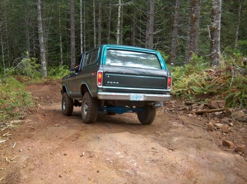 1978 Ford Bronco - A 1978 Ford Bronco navigates a wooded trail, showing its rear profile and lifted suspension.