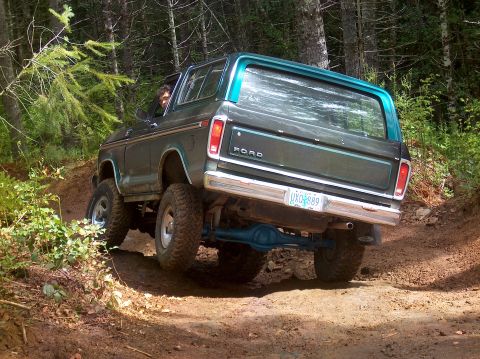 1978 Ford Bronco - A Ford Bronco navigates a wooded trail, kicking up dirt as it goes.