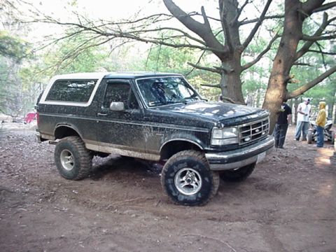 1993 Ford Bronco - A muddy Ford Bronco sits off-road with people gathered nearby.