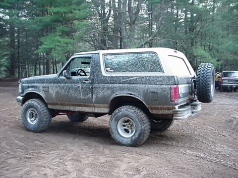1993 Ford Bronco - This 1993 Ford Bronco is shown in a three-quarter rear view, covered in mud, with a spare tire mounted on the tailgate.