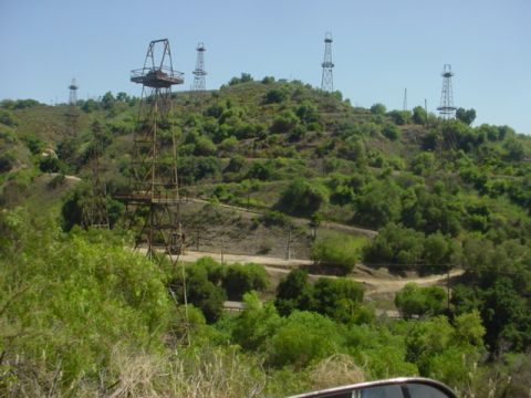 1988 Ford Bronco - Several oil derricks are visible on a vegetated hillside, with a dirt road winding through the terrain.