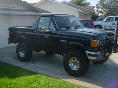 1988 Ford Bronco - A black Ford Bronco is parked in a driveway with other vehicles visible in the background.