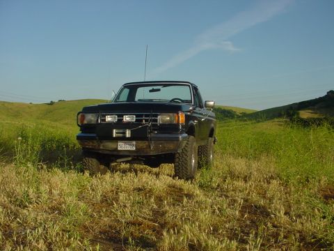 1988 Ford Bronco - A black pickup truck sits in a field of tall grass with rolling hills in the background.
