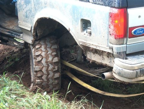 1979 Ford Bronco - A silver Ford Bronco is stuck in the mud, with a tow strap wrapped around its rear tire.