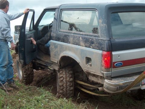 1979 Ford Bronco - A muddy 1979 Ford Bronco is stuck in the dirt, with one person entering the driver's side.