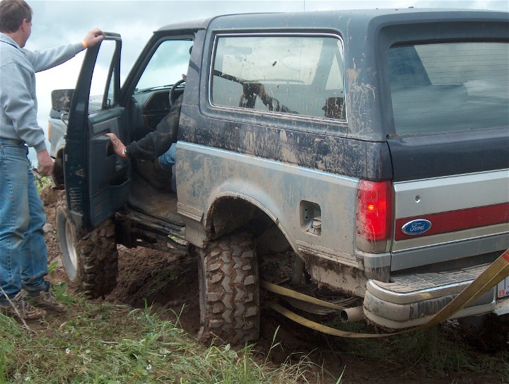 Muddy 1979 Ford Bronco stuck in dirt with a person entering