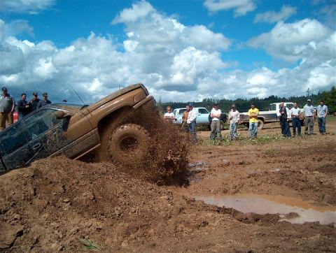 1979 Ford Bronco - A group of people watch as a brown SUV gets stuck in the mud during an off-road event.