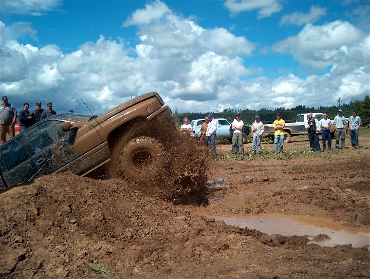 Brown SUV stuck in mud, splashing dirt, with spectators watching