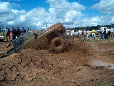 1979 Ford Bronco - Spectators watch as a brown SUV gets stuck deep in the mud during a mud bogging event.