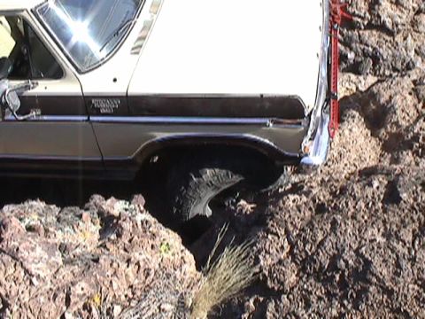 1979 Ford Bronco - Tight side view of the front fender and wheel of a cream and brown two-tone Ford Bronco with its front tire hanging into a rock crevice. A…
