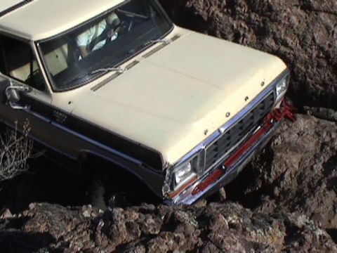 1979 Ford Bronco - Cream and dark two-tone Ford Bronco dropping nose-first into a rocky notch, shot from above the driver's front fender with the driver visib…