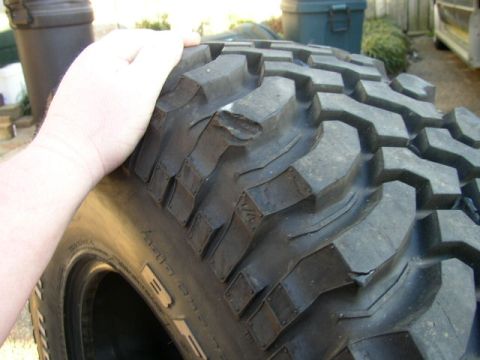 1995 Ford Bronco - A hand rests on a large, aggressive off-road tire, revealing its deep tread pattern and some wear.