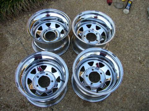 1995 Ford Bronco - A set of four polished chrome wheels are displayed on a rough surface, with some cleaning supplies in the background.