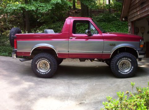 1995 Ford Bronco - This two-tone Ford Bronco is parked on a concrete driveway next to a wooded area.