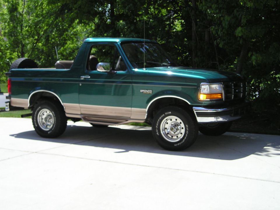 Green and tan Ford Bronco with hardtop removed, on BFGoodrich All-Terrain tires in a sunny driveway