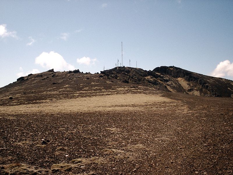 Barren volcanic mountain summit with antenna mast under blue sky