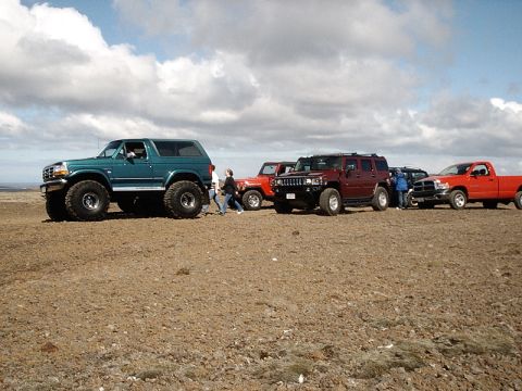 1996 Ford Bronco - Several off-road vehicles are lined up on a barren, rocky landscape under a cloudy sky.