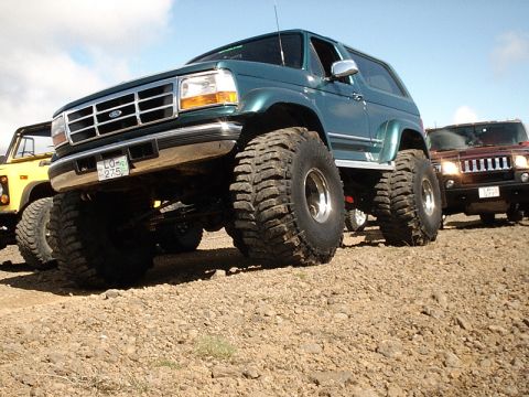 1996 Ford Bronco - A lifted green Ford Bronco is parked on a gravelly surface, with other vehicles visible in the background.