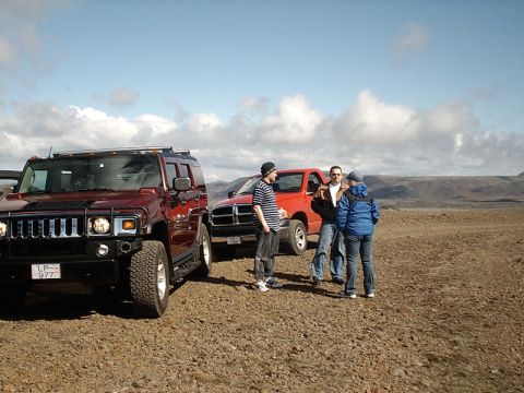 1996 Ford Bronco - Two trucks, a red Hummer H2 and a red Dodge Ram, are parked in a rocky, open landscape with three people standing between them.