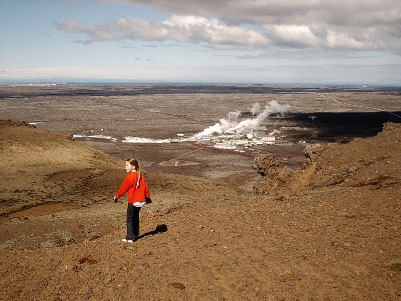 Child on volcanic hillside overlooking a steaming geothermal plant