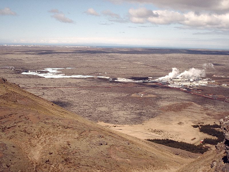 Aerial view of Icelandic lava plain with a steaming geothermal plant in the distance