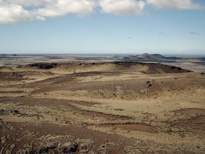Barren volcanic plain with cinder cones under a partly cloudy sky
