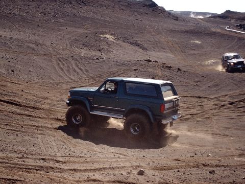 1996 Ford Bronco - Two SUVs navigate a dusty, off-road terrain with steep inclines and tire tracks.