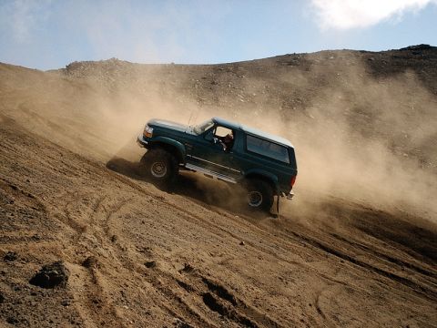 1996 Ford Bronco - This SUV is navigating a steep, dusty incline, creating a cloud of dirt as it ascends.
