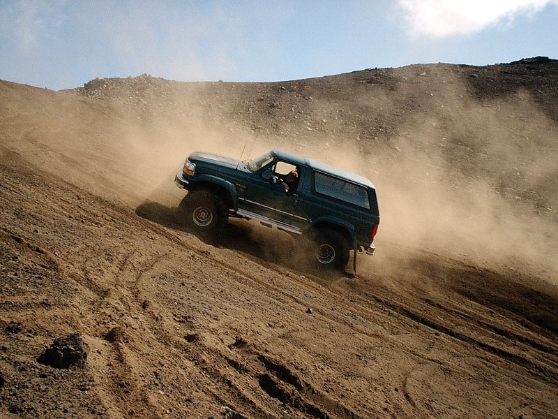 Dark green Ford Bronco SUV climbing a dusty dirt hill off-road