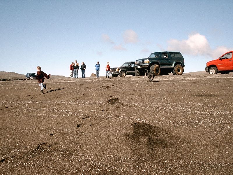 Dark green lifted Ford Bronco on gray volcanic plain with other vehicles and people