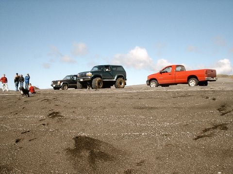 1996 Ford Bronco - Several vehicles and people are gathered on a sandy landscape under a partly cloudy sky.