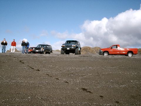 1996 Ford Bronco - Several vehicles, including a 1996 Ford Bronco, are parked on a sandy landscape under a cloudy sky.