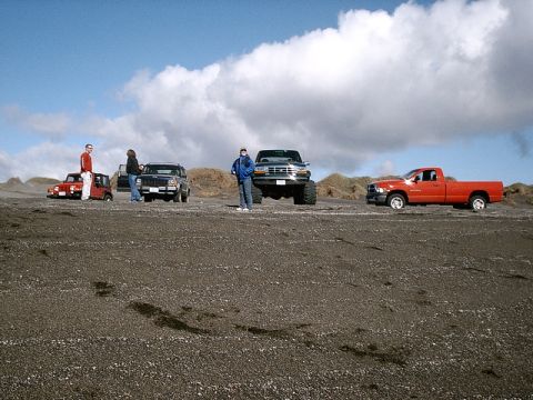 1996 Ford Bronco - Several vehicles are parked on a beach under a cloudy sky.
