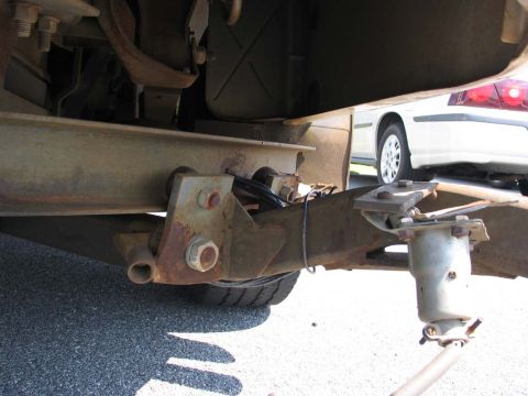 1995 Ford Bronco - Close-up view of a trailer hitch assembly attached to a vehicle's frame, with another car visible in the background.