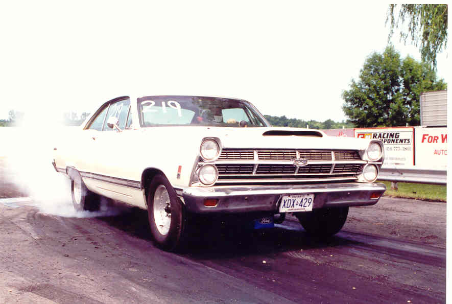 White Ford Fairlane hardtop doing a smoky burnout at the drag strip