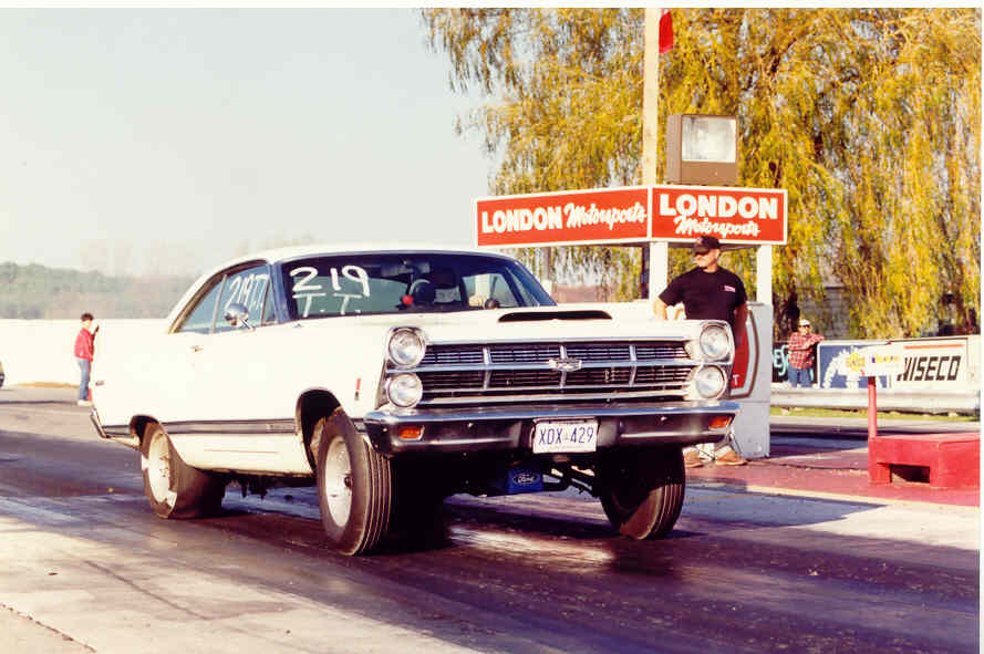 White 1967 Ford Fairlane drag car launching with front wheels up at a drag strip