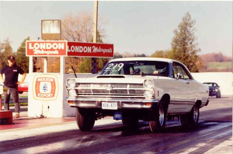 1967 Ford Fairlane - A white 1966 drag car with a hood scoop is seen from the front at a drag strip, with another car in the background.